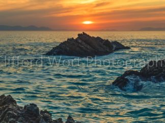 Rocky outcrops in the ocean with the sun setting behind