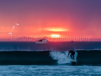 Surfer riding a wave during a storm lightening and thunder sunset